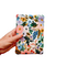 A hand holding a Kindle Paperwhite sleeve with snap to protect Kindle e-readers made with a pastel floral print atop a white background.
